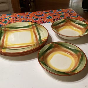 Könnte beinhalten: Set aus drei Keramiktellern mit einem grün-gelb-orangen Streifenmuster. Die Teller sind übereinander gestapelt.