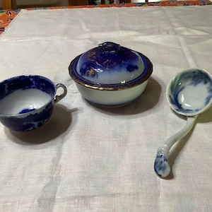 May include: A set of blue and white porcelain dishes with gold accents. The set includes a small bowl with a lid, a small cup, and a ladle.