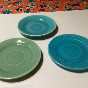 Pode incluir: Três pires de cerâmica em diferentes tons de azul e verde. Os pires são todos redondos e têm uma ligeira borda. São perfeitos para servir café ou chá.