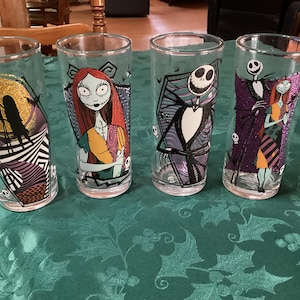 Puede incluir: Cuatro vasos transparentes con personajes de Pesadilla antes de Navidad. Los dise&ntilde;os incluyen a Jack Skellington y Sally en varias poses, con acentos coloridos en morado, naranja y amarillo, y patrones gr&aacute;ficos como rayas.