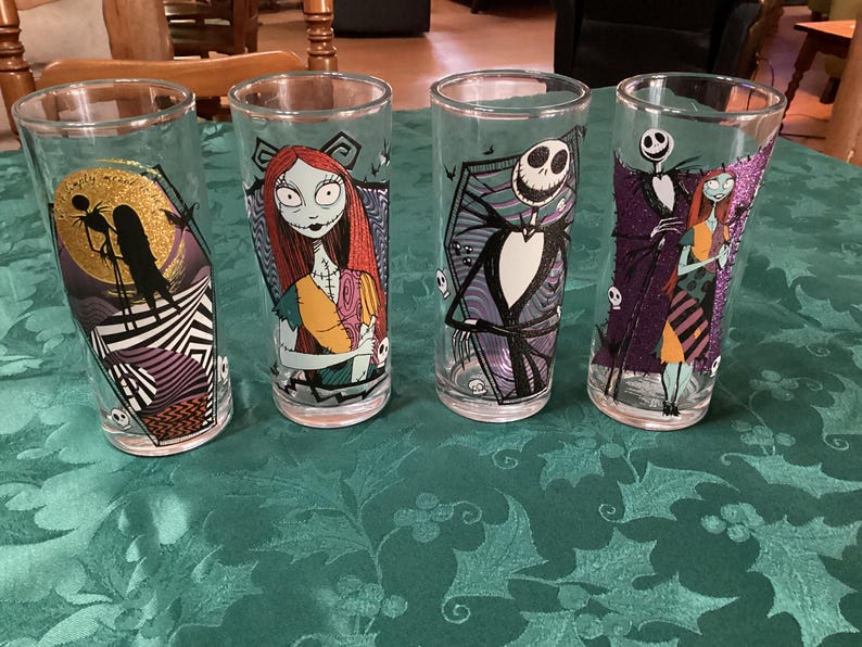 Puede incluir: Cuatro vasos transparentes con personajes de Pesadilla antes de Navidad. Los dise&ntilde;os incluyen a Jack Skellington y Sally en varias poses, con acentos coloridos en morado, naranja y amarillo, y patrones gr&aacute;ficos como rayas.