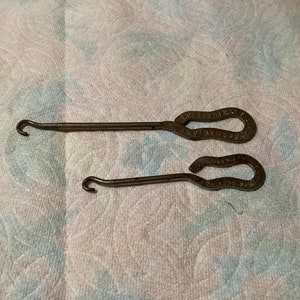 May include: Two antique metal shoe horn tools with a hook on one end and a loop on the other. The loop has the words "The Perfect Shoe Horn" engraved on it.