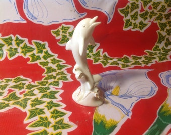 May include: White porcelain dolphin figurine with gold accents. The dolphin is leaping out of the water and has a detailed, realistic design.