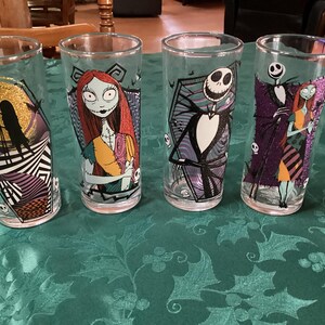 Puede incluir: Cuatro vasos de cristal transparente con personajes y escenas de Pesadilla antes de Navidad. Cada vaso muestra coloridos estampados gr&aacute;ficos de Jack Skellington y Sally, incluyendo una luna dorada con purpurina y motivos de calaveras.