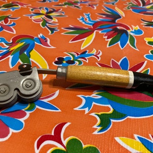 May include: A vintage can opener with a wooden handle and a silver metal cutting mechanism. The opener has two wheels with serrated edges for opening cans.