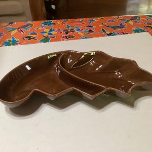 May include: A brown ceramic serving dish with two sections. The dish is shaped like a leaf and has a glossy finish.