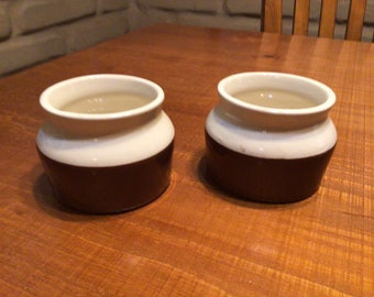May include: Two brown and white ceramic cups with a white rim and a brown base. The cups are filled with a light brown liquid.