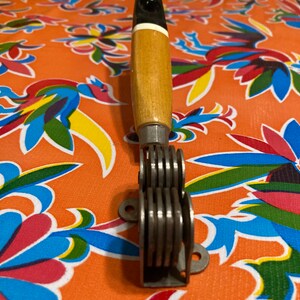 May include: A vintage knife sharpener with a wooden handle and a metal sharpening mechanism. The handle is black and white with a wood grain pattern. The sharpening mechanism has multiple metal blades.