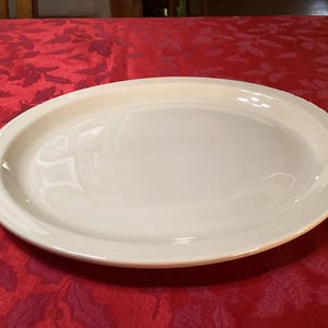 May include: A white oval serving platter with a slightly raised rim. The platter is made of ceramic and has a smooth, glossy finish.