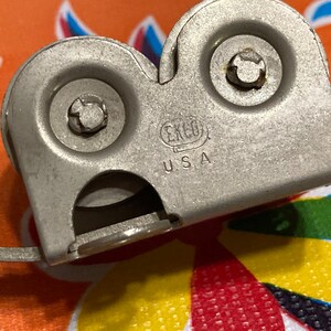 May include: A silver metal can opener with two wheels and a handle. The can opener has the text "EKCO U.S.A." on it.