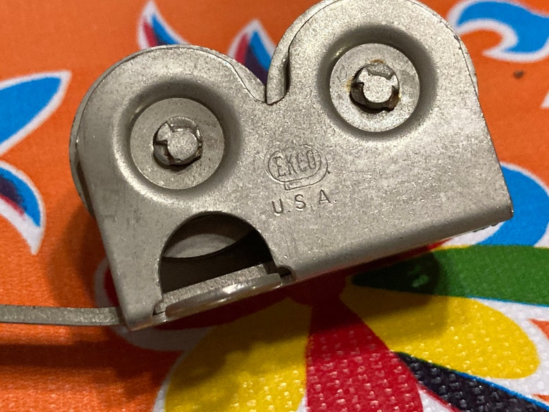 May include: A silver metal can opener with two wheels and a handle. The can opener has the text "EKCO U.S.A." on it.