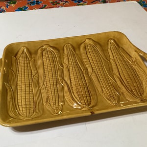 Puede incluir: Un plato de servir de cerámica amarillo con cinco moldes de mazorcas de maíz. El plato tiene dos asas a los lados.