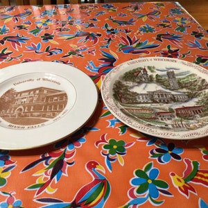 May include: Two decorative plates featuring the University of Wisconsin. One plate is white with a gold rim and a sepia-toned image of a building. The other plate has a detailed illustration of campus buildings.
