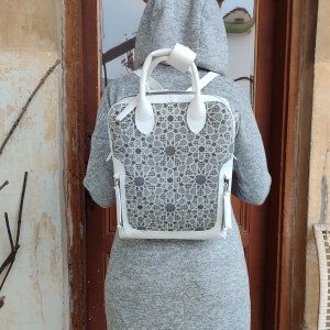 May include: A white leather backpack with a geometric pattern. The backpack has a top handle and adjustable straps.