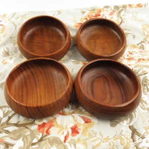 May include: Four round wooden bowls with a rich brown color and visible wood grain. The bowls are set on a floral patterned fabric. The bowls have a smooth, polished finish and a simple, classic design.