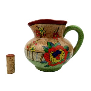 May include: A vintage ceramic pitcher with a green handle and floral design. The pitcher has a crackled glaze and is decorated with red, yellow, and blue flowers.