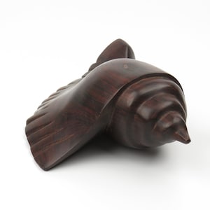 May include: A dark brown wooden sculpture of a seashell. The sculpture is carved in a realistic style and has a smooth, polished finish.