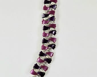 May include: A vintage bracelet featuring alternating dark purple and light purple enamel bow-shaped links. The links are connected by silver-toned metal. The bracelet has a clasp closure. The jewelry is displayed on a white background.