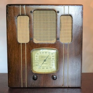 May include: A vintage wooden radio with a dial that reads "BROADCAST" and has numbers from 65 to 450. The radio has a brown wooden cabinet with a light brown grill.