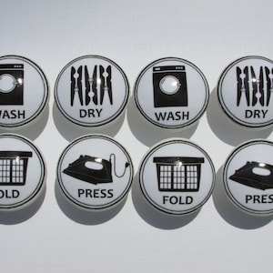 May include: Eight white ceramic knobs with black laundry symbols. The symbols include a washing machine, clothes drying rack, laundry basket, and iron. The words "WASH", "DRY", "FOLD", and "PRESS" are printed on the knobs.