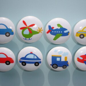 May include: Eight white round knobs with colorful cartoon images of vehicles, including a blue car, a green helicopter, a blue airplane, a yellow taxi, a red car, a blue police car, a blue train, and a red airplane.