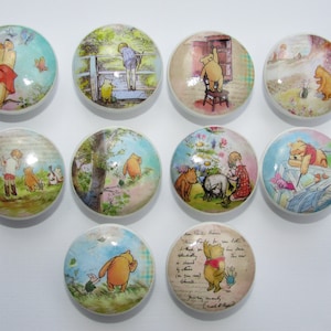May include: Ten round ceramic knobs with Winnie the Pooh characters and scenes from the book. The knobs are white with a glossy finish. The scenes include Winnie the Pooh with Piglet, Winnie the Pooh with Tigger, Winnie the Pooh with Eeyore, Winnie the Pooh with Christopher Robin, and Winnie the Pooh with a bee.