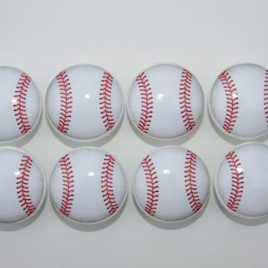 May include: Eight white ceramic cabinet knobs with a baseball design. The baseballs are white with red stitching.