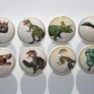 May include: Set of eight round ceramic knobs featuring different dinosaur illustrations. Each knob has a white background with a vintage-style design. The dinosaurs are depicted in various poses and colors, including green, brown, blue, and gray.