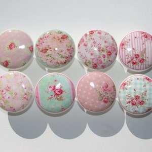 May include: Eight round, white ceramic knobs with a variety of floral patterns in pink, green, and blue. The patterns include polka dots, stripes, and floral bouquets.