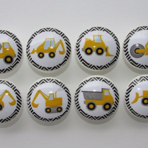 May include: Eight yellow construction vehicle themed knobs with black and white chevron patterns. The knobs feature a dump truck, bulldozer, excavator, backhoe, and a steamroller.