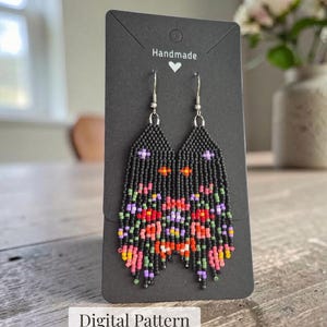 Könnte beinhalten: Ein Paar Ohrringe aus schwarzen Saatperlen mit einem Blumenmuster in Rot-, Rosa-, Lila-, Orange- und Grüntönen. Die Ohrringe sind auf einer schwarzen Karte mit dem Text Handmade und einem Herzsymbol sowie dem Text Digital Pattern befestigt.