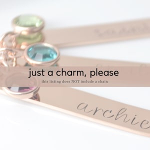 May include: Gold charm necklace with three personalized nameplate charms. The charms are engraved with the names "Sophia", "Lily", and "Archie". The necklace is adorned with three colorful gemstones: green, blue, and purple.