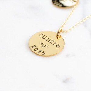 Puede incluir: Collar de oro con un colgante redondo que dice "auntie est 2025".