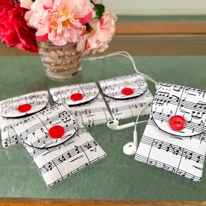 May include: Five white fabric pouches with black trim and red buttons. Each pouch features a musical note pattern and is designed to hold small items like earbuds or other accessories.
