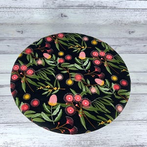 May include: Round black fabric with a floral pattern featuring pink and yellow flowers and green leaves.