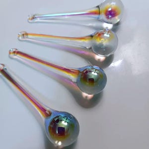 May include: Four iridescent glass ornaments with a teardrop shape and a spherical bulb at the end. The glass reflects a rainbow of colors, including yellow, orange, and blue. The ornaments are arranged diagonally.