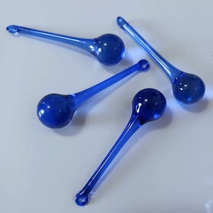 May include: Four cobalt blue glass ornaments with a teardrop shape and a small loop at the end. The ornaments have a long, slender stem leading to a round bulb. The glass is transparent and reflects light.