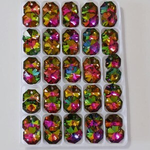 May include: A tray filled with iridescent, multi-faceted crystal rhinestones. The crystals are arranged in a grid pattern, showcasing a spectrum of colors including green, pink, yellow, and purple. Each crystal has a rectangular shape with beveled edges.