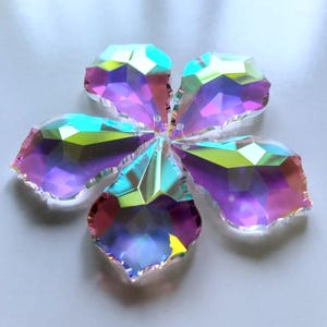 May include: A flower-shaped crystal pendant with five iridescent petals. The petals are faceted, displaying a range of colors including purple, pink, green, and blue. The crystal is designed to catch and reflect light.
