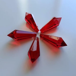 May include: Five faceted, red crystal pendants arranged in a starburst pattern. Each pendant is a deep, transparent red with multiple cut surfaces, catching and reflecting light. The pendants are likely for jewelry making or decorative purposes.