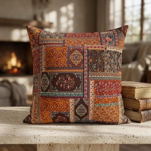 May include: A square throw cushion featuring a patchwork design with various rectangular panels. The fabric displays a mix of orange, red, brown, and muted blue tones with intricate floral, paisley, and geometric patterns throughout the surface.