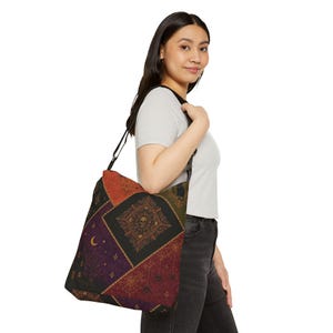 May include: A crossbody tote bag featuring a patchwork design with dark, gothic-inspired patterns including a skull, spiderwebs, a crescent moon, and ornate floral motifs in shades of black, deep red, purple, and orange with a black shoulder strap.