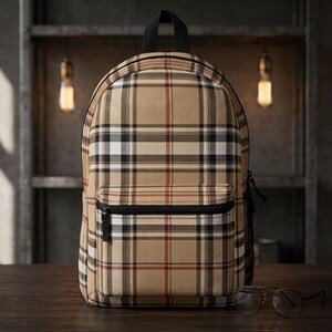 Puede incluir: Una mochila de color beige con un patrón de cuadros clásico en rayas negras, blancas y rojas. La bolsa incluye un asa superior, un bolsillo frontal con cremallera y tirador negro, y bolsillos laterales de malla negra. Unas gafas negras están delante.