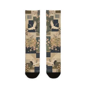 May include: A pair of crew socks featuring a repeating pattern of white cranes in flight, pink cherry blossoms, and green bamboo stalks set against a background of dark blue and beige geometric blocks with black toe and heel sections.