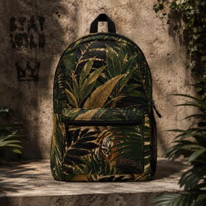 May include: A backpack featuring a dark green and black tropical leaf pattern with a tiger face partially visible on the front pocket. The bag includes a top handle, a zippered front compartment, and black side mesh pockets for storage.