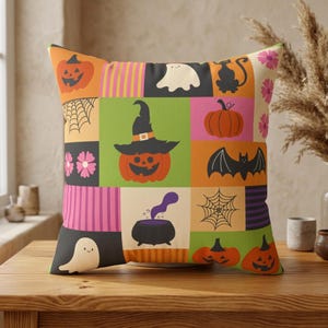 May include: A square throw pillow featuring a patchwork design with Halloween-themed illustrations including jack-o'-lanterns, a ghost, a black cat, a bat, a spider web, a witch's hat, and a bubbling cauldron, accented by pink flowers and stripes.