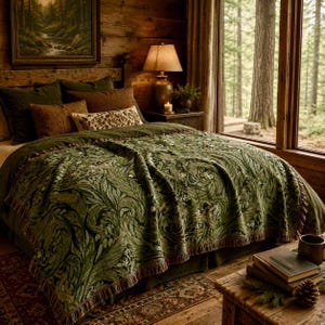 May include: A woven throw blanket featuring a dark green botanical pattern with swirling leaves and small white flowers, finished with a fringed edge. The blanket is draped over a bed with dark green and brown pillows in a rustic bedroom setting.