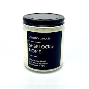 May include: A clear glass candle jar with a black lid and label. The label reads "LOSTBIRCH CANDLES SHERLOCK'S HOME Cedar Amber Woods 8 oz natural soy candle handpoured in MN".