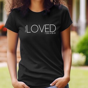 Może przedstawiać: Czarny T-shirt z białym napisem "You are LOVED 1 John 4:18-19".