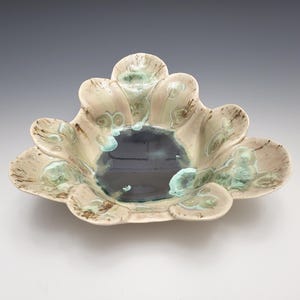 May include: A ceramic bowl with a unique, scalloped design. The bowl features a dark blue center and is surrounded by petal-like edges in a beige hue, accented with green and brown details. This decorative piece is ideal for serving or display.